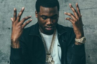 A man with his hands raised in the air, expressing a sense of surrender or celebration. Image from the music video "Otherside of America" by Meek Mill