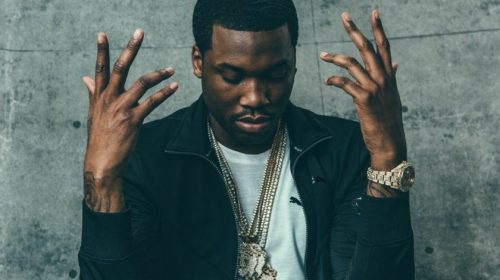 A man with his hands raised in the air, expressing a sense of surrender or celebration. Image from the music video "Otherside of America" by Meek Mill